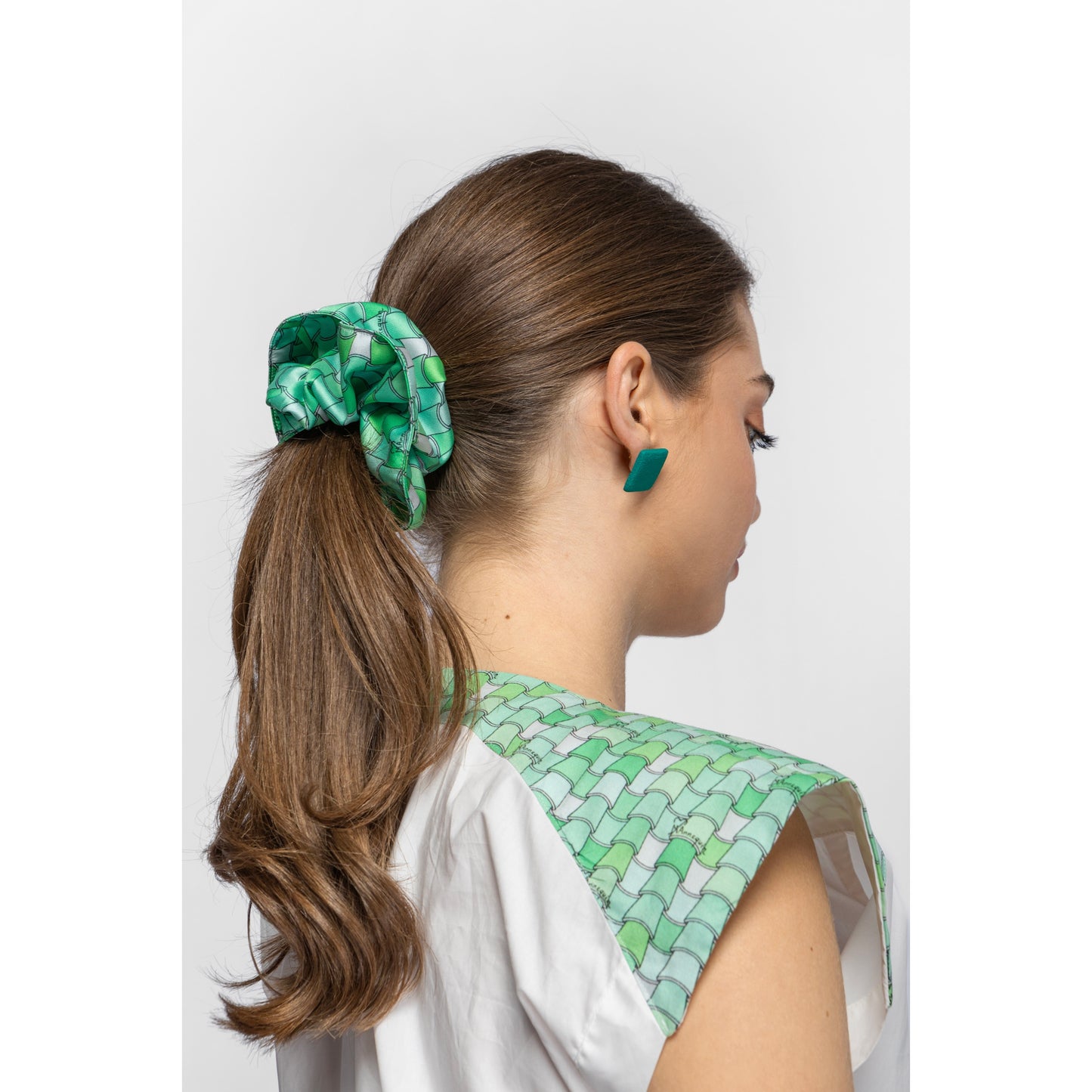 Woman wearing a green patterned scrunchie and earrings against a white background